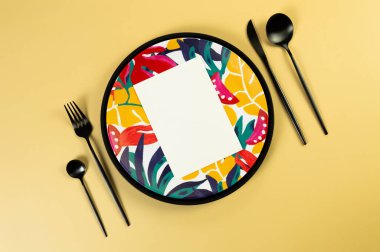 Siyah tepsinin üst görüntüsü, renkli tabaklar, sarı arka planda siyah çatal bıçak takımı. Beyaz kart, egzotik bitki tabağı, yaz pikniği. Düz yat, boşluğu kopyala.