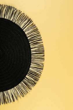 Sarı arkaplandaki siyah hasır masa örtüsünün üst görüntüsü. Saman yuvarlak tepsi, düz konum, kopyalama alanı. 