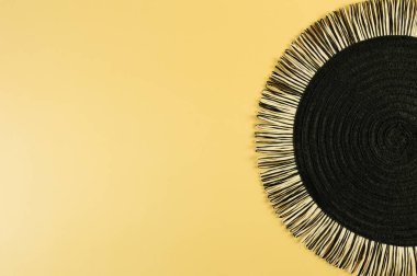 Sarı arkaplandaki siyah hasır masa örtüsünün üst görüntüsü. Saman yuvarlak tepsi, düz konum, kopyalama alanı. 