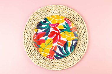 Kahverengi hasır masa paspasının üst görüntüsü, pembe arka planda renkli plaka. Saman tepsisi, egzotik bitki tabağı, yaz pikniği. Düz yat, boşluğu kopyala.