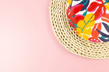 Kahverengi hasır masa paspasının üst görüntüsü, pembe arka planda renkli plaka. Saman tepsisi, egzotik bitki tabağı, yaz pikniği. Düz yat, boşluğu kopyala.