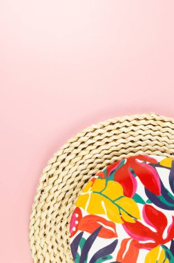 Kahverengi hasır masa paspasının üst görüntüsü, pembe arka planda renkli plaka. Saman tepsisi, egzotik bitki tabağı, yaz pikniği. Düz yat, boşluğu kopyala.