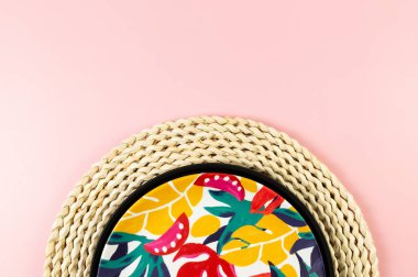 Kahverengi hasır masa paspası, siyah tepsi ve pembe arka planda renkli plaka. Saman tepsisi, egzotik bitki tabağı, yaz pikniği. Düz yat, boşluğu kopyala.