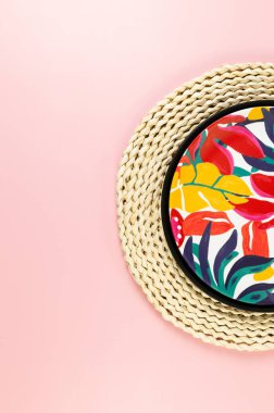 Kahverengi hasır masa paspası, siyah tepsi ve pembe arka planda renkli plaka. Saman tepsisi, egzotik bitki tabağı, yaz pikniği. Düz yat, boşluğu kopyala.