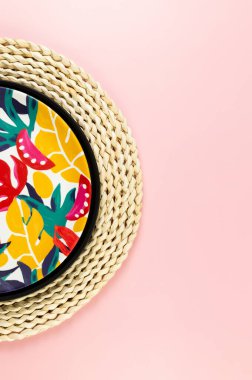 Kahverengi hasır masa paspası, siyah tepsi ve pembe arka planda renkli plaka. Saman tepsisi, egzotik bitki tabağı, yaz pikniği. Düz yat, boşluğu kopyala.