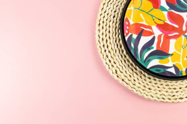 Kahverengi hasır masa paspası, siyah tepsi ve pembe arka planda renkli plaka. Saman tepsisi, egzotik bitki tabağı, yaz pikniği. Düz yat, boşluğu kopyala.
