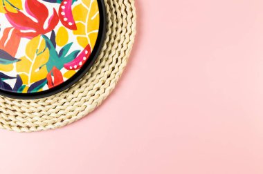 Kahverengi hasır masa paspası, siyah tepsi ve pembe arka planda renkli plaka. Saman tepsisi, egzotik bitki tabağı, yaz pikniği. Düz yat, boşluğu kopyala.
