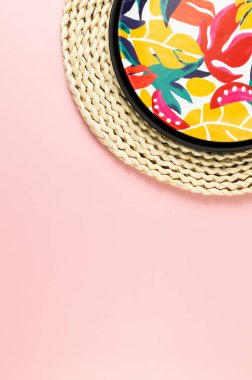 Kahverengi hasır masa paspası, siyah tepsi ve pembe arka planda renkli plaka. Saman tepsisi, egzotik bitki tabağı, yaz pikniği. Düz yat, boşluğu kopyala.