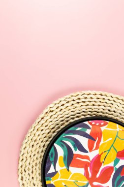 Kahverengi hasır masa paspası, siyah tepsi ve pembe arka planda renkli plaka. Saman tepsisi, egzotik bitki tabağı, yaz pikniği. Düz yat, boşluğu kopyala.