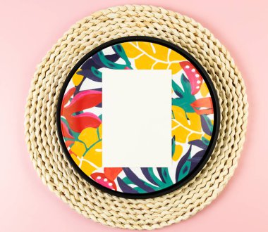 Kahverengi hasır masa paspası, beyaz kart, siyah tepsi ve pembe arka planda renkli tabak. Saman tepsisi, egzotik bitki tabağı, yaz pikniği. Düz yat, boşluğu kopyala.