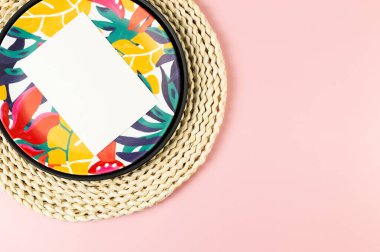 Kahverengi hasır masa paspası, beyaz kart, siyah tepsi ve pembe arka planda renkli tabak. Saman tepsisi, egzotik bitki tabağı, yaz pikniği. Düz yat, boşluğu kopyala.