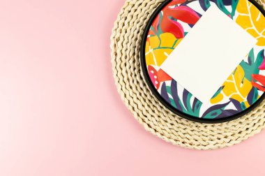 Kahverengi hasır masa paspası, beyaz kart, siyah tepsi ve pembe arka planda renkli tabak. Saman tepsisi, egzotik bitki tabağı, yaz pikniği. Düz yat, boşluğu kopyala.