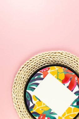 Kahverengi hasır masa paspası, beyaz kart, siyah tepsi ve pembe arka planda renkli tabak. Saman tepsisi, egzotik bitki tabağı, yaz pikniği. Düz yat, boşluğu kopyala.