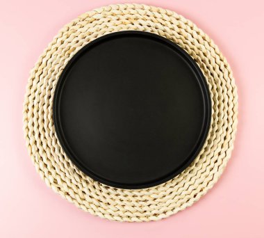 Kahverengi hasır masa paspası, pembe arka planda siyah plaka. Saman yuvarlak tepsi, düz konum, kopyalama alanı.