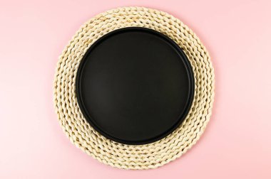 Kahverengi hasır masa paspası, pembe arka planda siyah plaka. Saman yuvarlak tepsi, düz konum, kopyalama alanı.