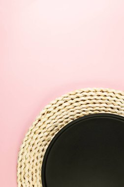 Kahverengi hasır masa paspası, pembe arka planda siyah plaka. Saman yuvarlak tepsi, düz konum, kopyalama alanı.