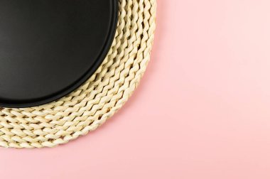 Kahverengi hasır masa paspası, pembe arka planda siyah plaka. Saman yuvarlak tepsi, düz konum, kopyalama alanı.