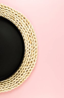 Kahverengi hasır masa paspası, pembe arka planda siyah plaka. Saman yuvarlak tepsi, düz konum, kopyalama alanı.