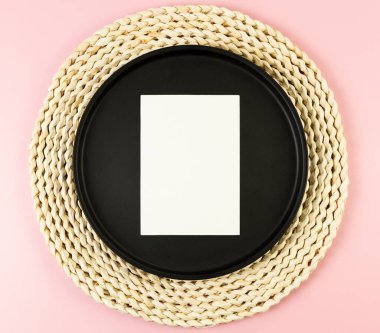 Kahverengi hasır masa paspası, siyah plaka, pembe arka planda beyaz kart. Saman yuvarlak tepsi, düz konum, kopyalama alanı.