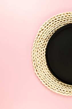 Kahverengi hasır masa paspası, pembe arka planda siyah plaka. Saman yuvarlak tepsi, düz konum, kopyalama alanı.