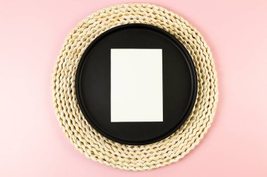 Kahverengi hasır masa paspası, siyah plaka, pembe arka planda beyaz kart. Saman yuvarlak tepsi, düz konum, kopyalama alanı.