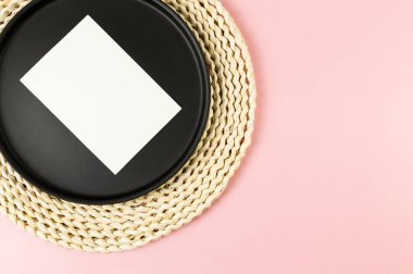 Kahverengi hasır masa paspası, siyah plaka, pembe arka planda beyaz kart. Saman yuvarlak tepsi, düz konum, kopyalama alanı.