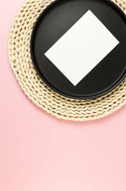 Kahverengi hasır masa paspası, siyah plaka, pembe arka planda beyaz kart. Saman yuvarlak tepsi, düz konum, kopyalama alanı.