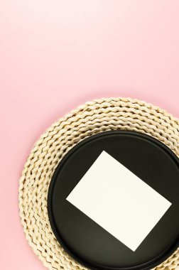 Kahverengi hasır masa paspası, siyah plaka, pembe arka planda beyaz kart. Saman yuvarlak tepsi, düz konum, kopyalama alanı.