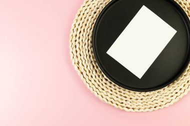 Kahverengi hasır masa paspası, siyah plaka, pembe arka planda beyaz kart. Saman yuvarlak tepsi, düz konum, kopyalama alanı.