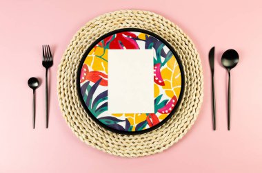 Kahverengi hasır masa paspası, renkli tabak, pembe arka planda siyah çatal bıçak. Siyah tepsi, beyaz kart, saman yuvarlak tepsi, egzotik bitki plakası. Yaz pikniği, düz yatak, kopyalama alanı.