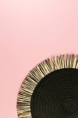 Pembe arkaplandaki siyah hasır masa örtüsünün üst görüntüsü. Saman yuvarlak tepsi, düz konum, kopyalama alanı.