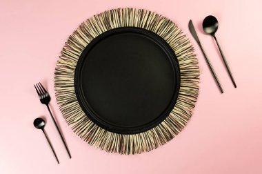 Siyah hasır masa paspası, sarı arka planda siyah çatal bıçak takımı. Saman yuvarlak tepsi, düz konum, kopyalama alanı.