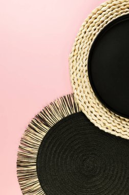 Kahverengi hasır masa paspası, siyah plaka, pembe arka planda siyah tepsi. Saman yuvarlak tepsi, düz konum, kopyalama alanı.