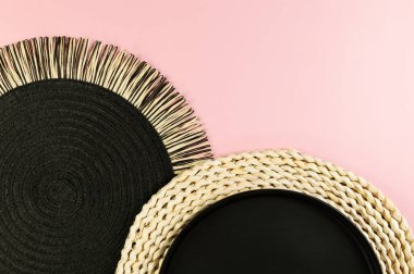 Kahverengi hasır masa paspası, siyah plaka, pembe arka planda siyah tepsi. Saman yuvarlak tepsi, düz konum, kopyalama alanı.