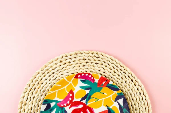 Kahverengi hasır masa paspasının üst görüntüsü, pembe arka planda renkli plaka. Saman tepsisi, egzotik bitki tabağı, yaz pikniği. Düz yat, boşluğu kopyala.