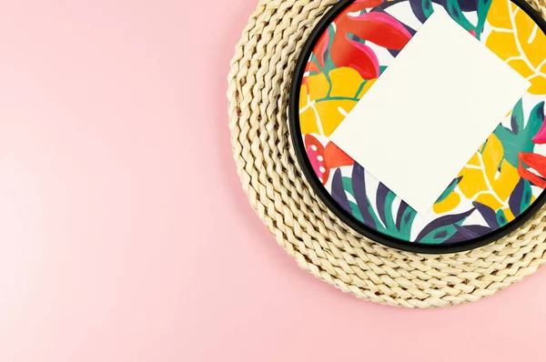 Kahverengi hasır masa paspası, beyaz kart, siyah tepsi ve pembe arka planda renkli tabak. Saman tepsisi, egzotik bitki tabağı, yaz pikniği. Düz yat, boşluğu kopyala.