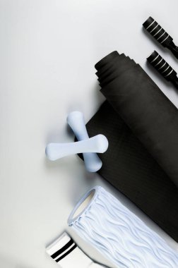 Mavi halterlerin üst görüntüsü, mavi masaj silindiri, siyah atlama ipi ve gri arka planda yuvarlanmış yoga minderi. Beyaz spor çoraplar, spor, spor, spor ve sağlık. Düz yat, boşluğu kopyala.