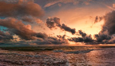 Gökyüzündeki dramatik ışıklar ve okyanusun üzerindeki gün batımındaki kötü hava koşulları kara kümülüs bulutları ile su arasındaki güzel güneş ışınları yansımaları ile kıyıya vuran dalgaları tehdit ediyor.
