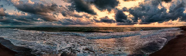 激しい積乱雲と海の水の間に美しい太陽の光の反射と曇りの黄金の空で海岸にクラッシュ波を脅かす海の上に劇的な天気パノラマ — ストック写真
