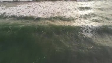 Güneş ışınlarının hava görüntüsü, zümrüt rengi su ve beyaz köpükle köpüren okyanus dalgalarını vurur.