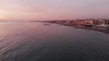 Ostia lido 'daki Roma kıyı şeridindeki hava günbatımı. Şehir silüeti ve sakin su.
