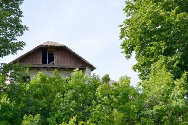 Doğal arka planda terk edilmiş güzel bir çiftlik evi. Fotoğraf, yabani otların oradaki terk edilmiş çiftlik evinden oluşuyor. Gökyüzünde terk edilmiş eski bir çiftlik evi..