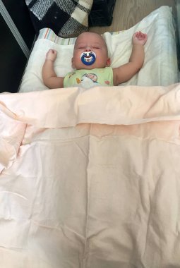 Çocuk emziği ile uyuyan bebek fotoğrafçı renkli fotoğraf için poz veriyor. Bebek emziğinden uyuyan bir oğlan çocuğu, gülen surat. Çocuk emziğinde sağlıklı uyuyan bebek..