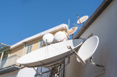 Sinyal iletimi için temel parçalar olan bir grup uydu antenleri çok katlı bir binanın yan tarafında yer almaktadır.