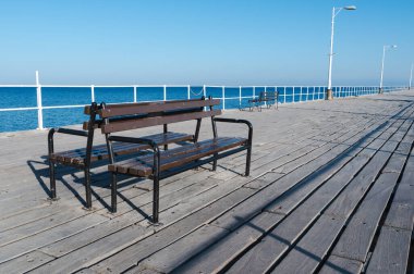 A serene view of a rustic wooden bench on a pier, overlooking calm blue waters and clear skies in an idyllic landscape