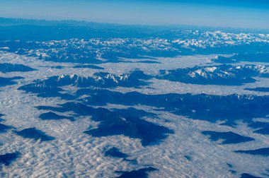 Görkemli, karla kaplı dağların engin bulut denizinin üzerinde yükseldiği çarpıcı bir hava manzarasına tanık olun.