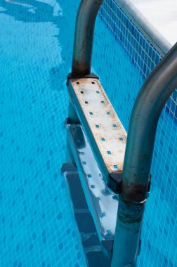 Ferahlatıcı ve temiz bir yüzme havuzuna inen paslı, eski bir merdivenin detaylı bir yakın çekimi.