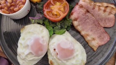 Yumurta, kıtır pastırma, lezzetli fasulye ve yanında taze salata içeren doyurucu bir kahvaltı tabağı.