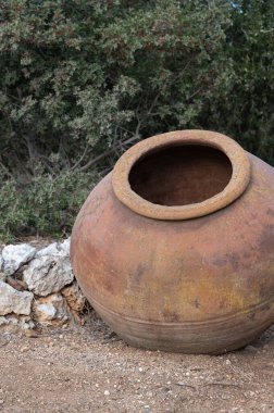 Yeşilliklerle çevrili, taştan bir duvara yaslanmış antik bir çömlek kırsal cazibesini ön plana çıkarıyor.