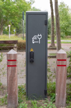 Açık hava elektrikli araç park yolunda Bollards yanında duruyor, mat gri metal kutu beyaz buji ve araba ikonu ile işaretli, yıpranmış kilit,